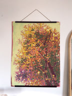 Framed painting of a tree with autumn foliage on a white wall.