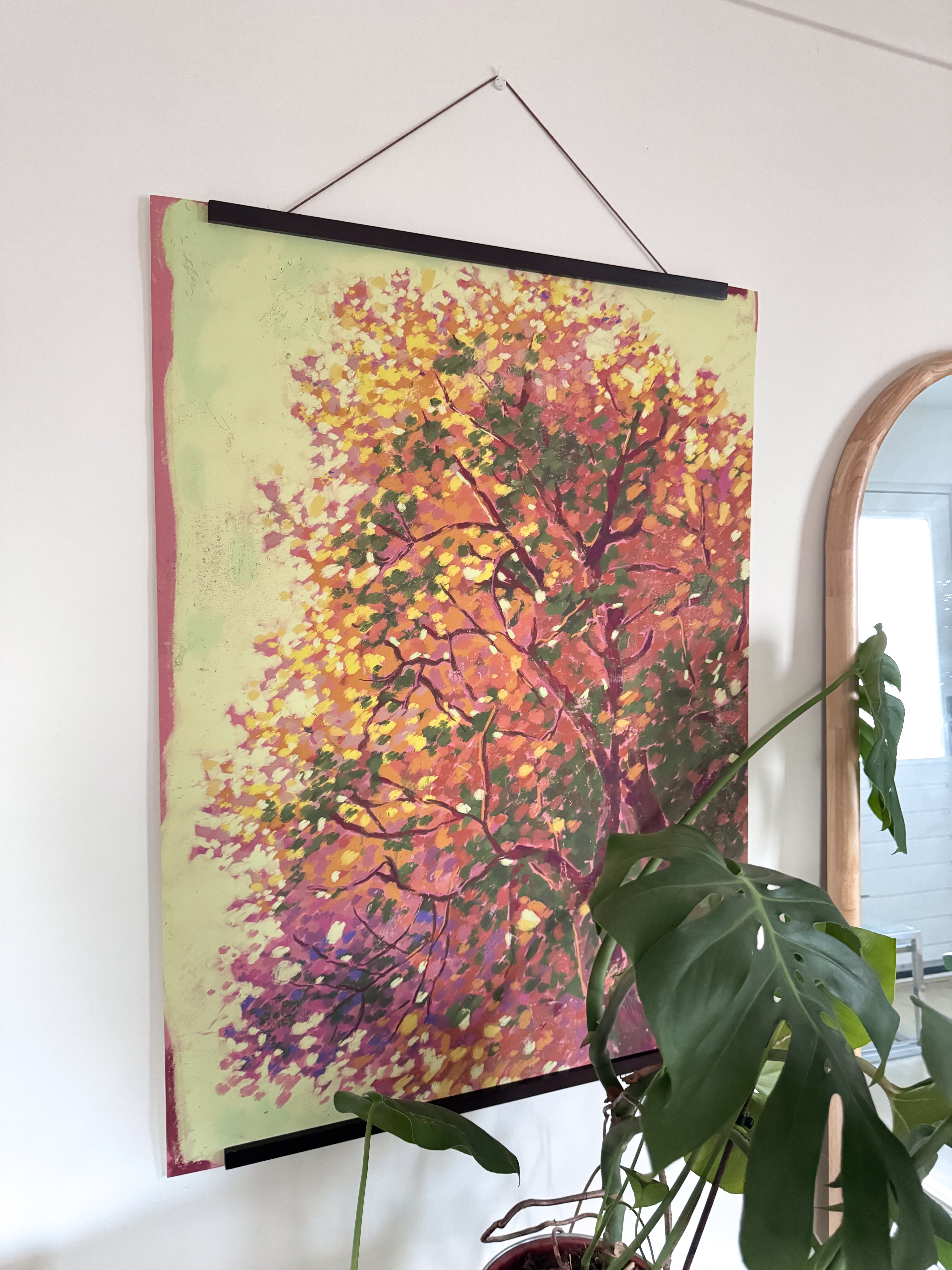 Colorful tree art print hanging on a wall with a plant in the foreground.