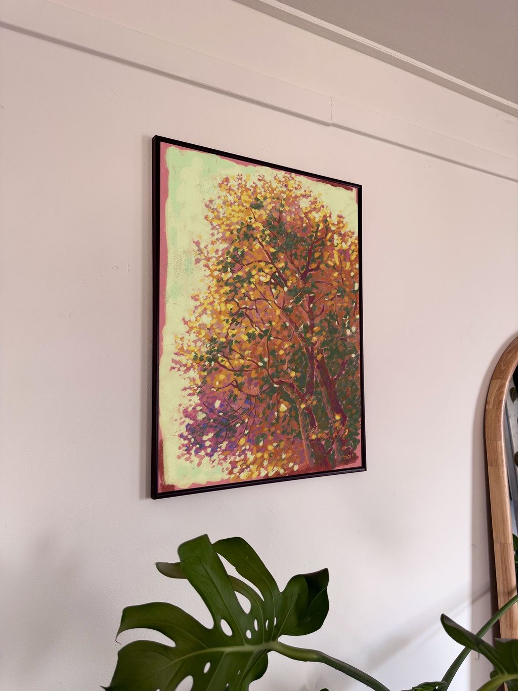 Framed abstract painting of a tree on a wall with a plant in the foreground