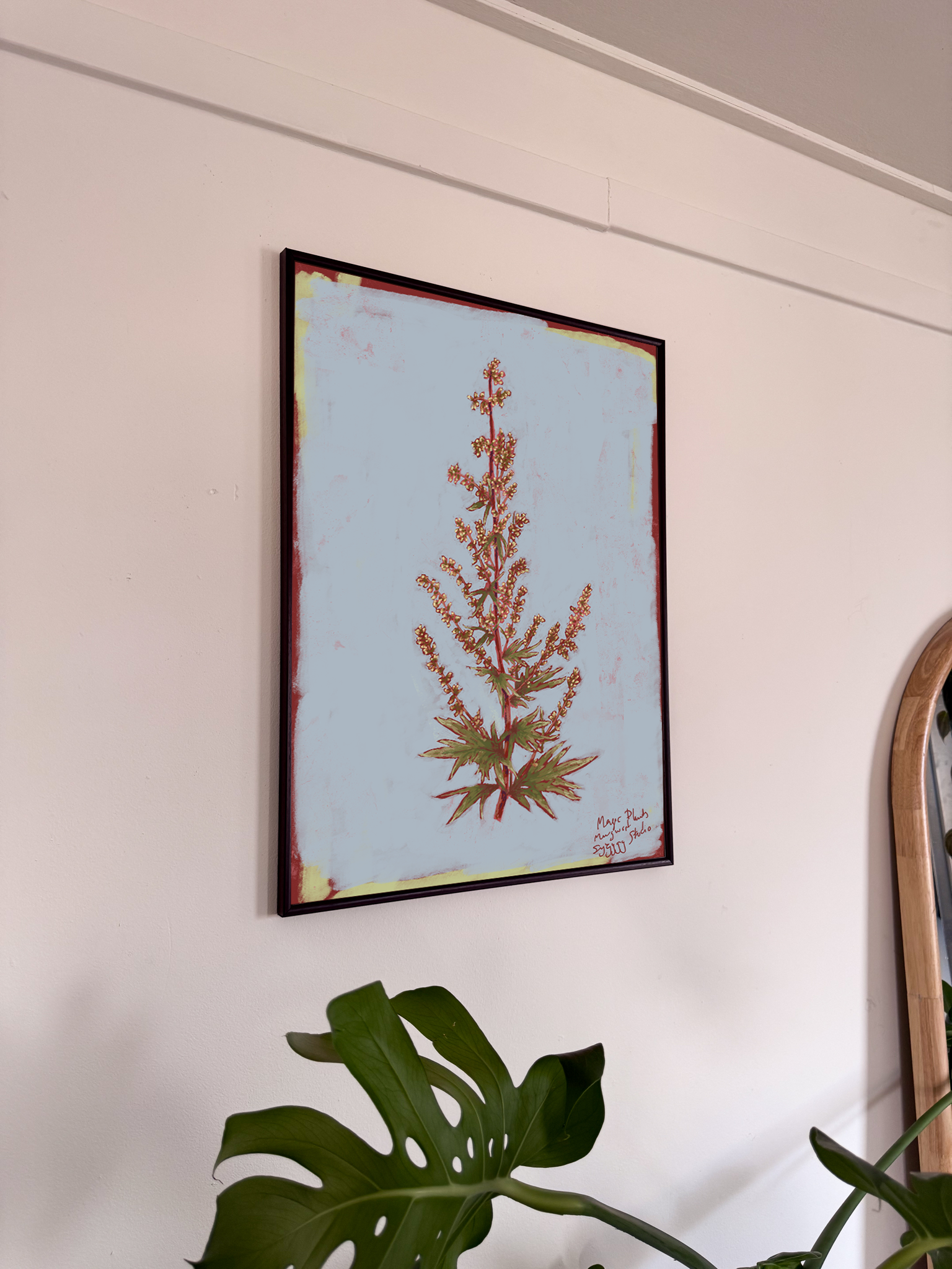 Framed botanical artwork on a wall with a plant in the foreground