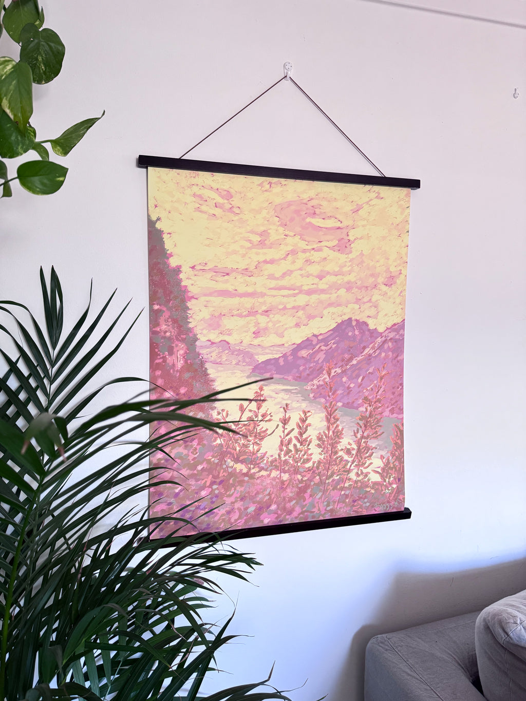Wall art with hanger, with a pink and yellow abstract design hanging on a white wall.
