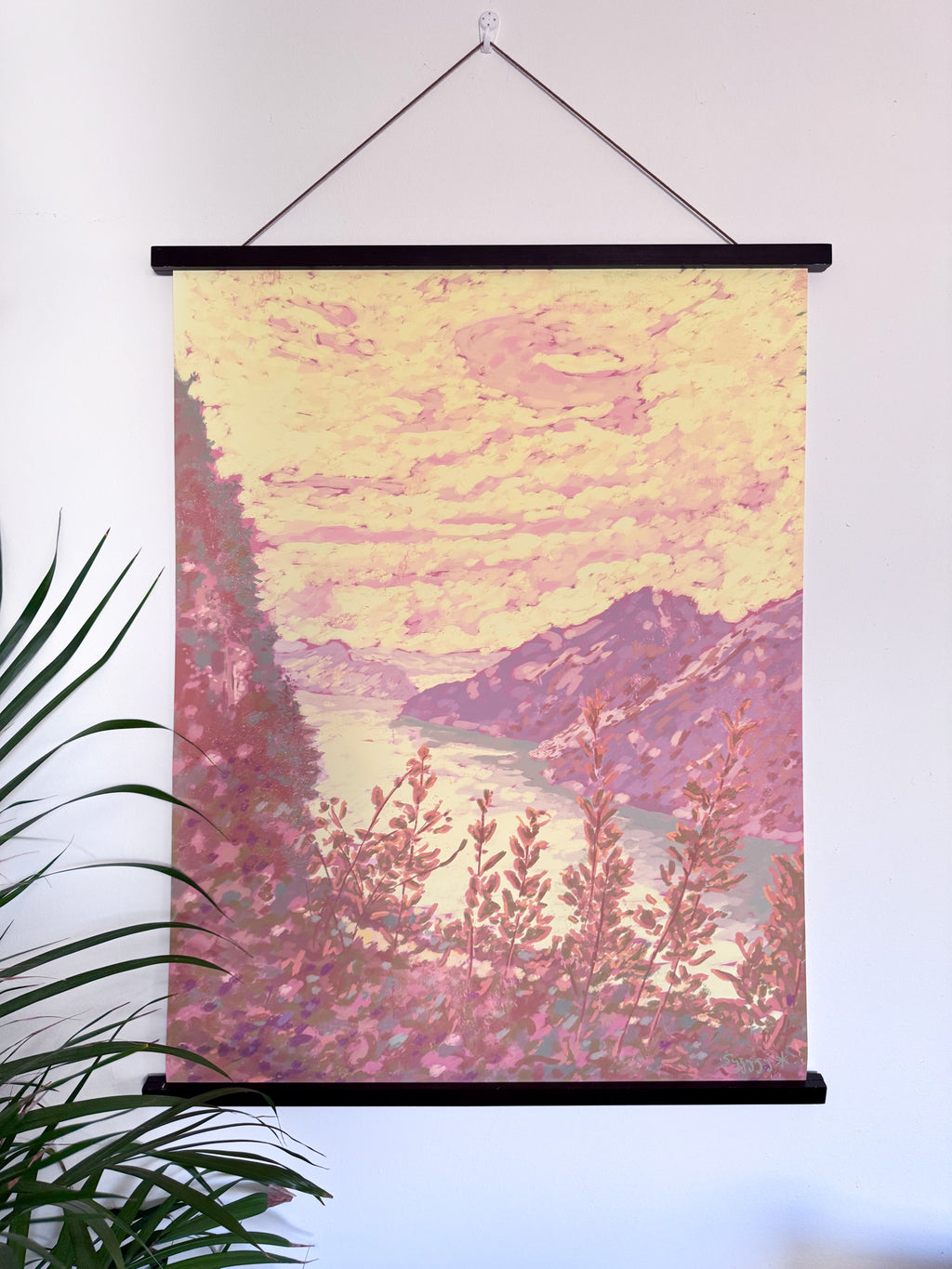 Roll-up landscape poster with pink and purple hues of a mountain and lake scene, hanging on a wall.