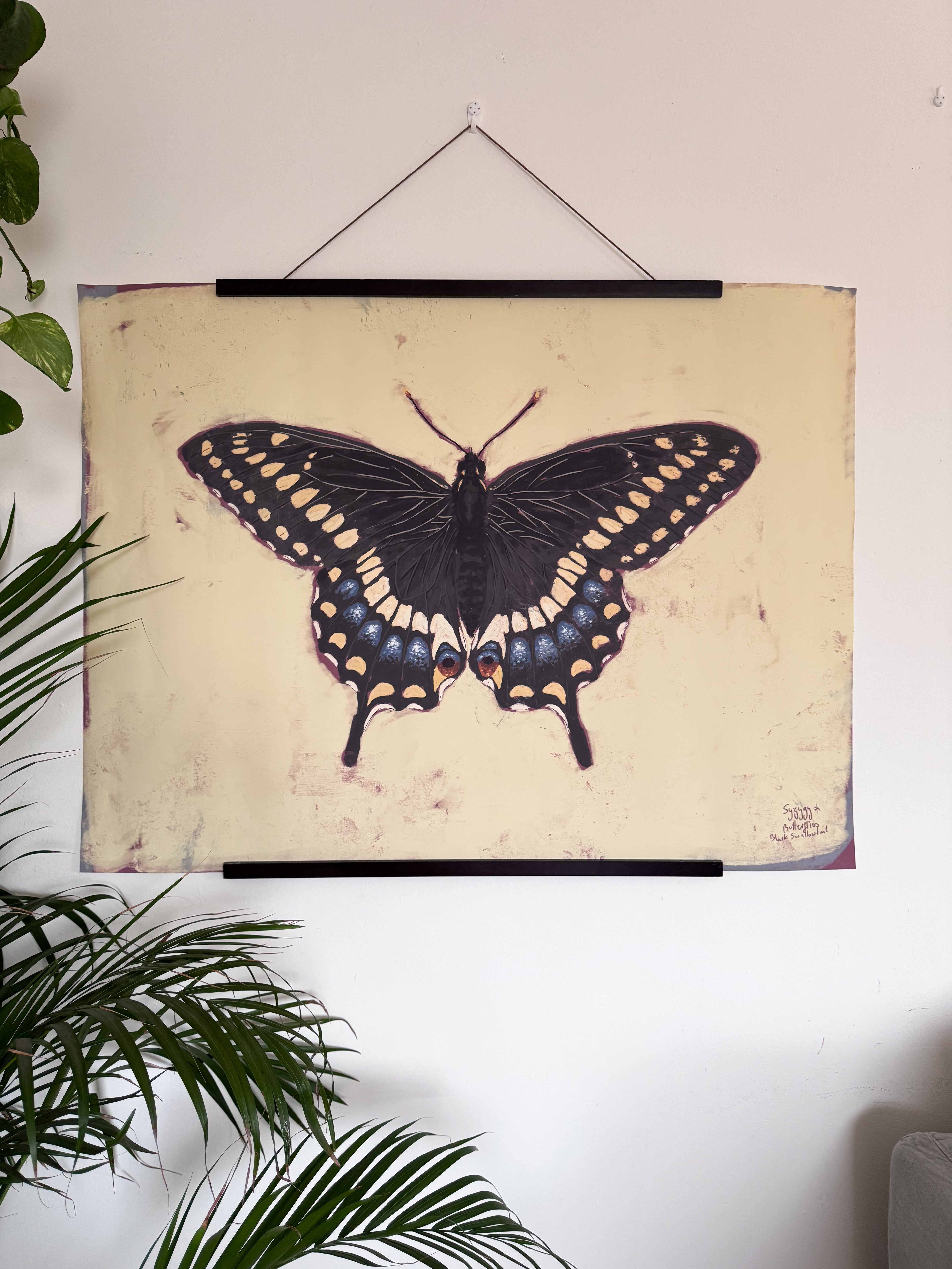 Black butterfly poster on a wall with plants around