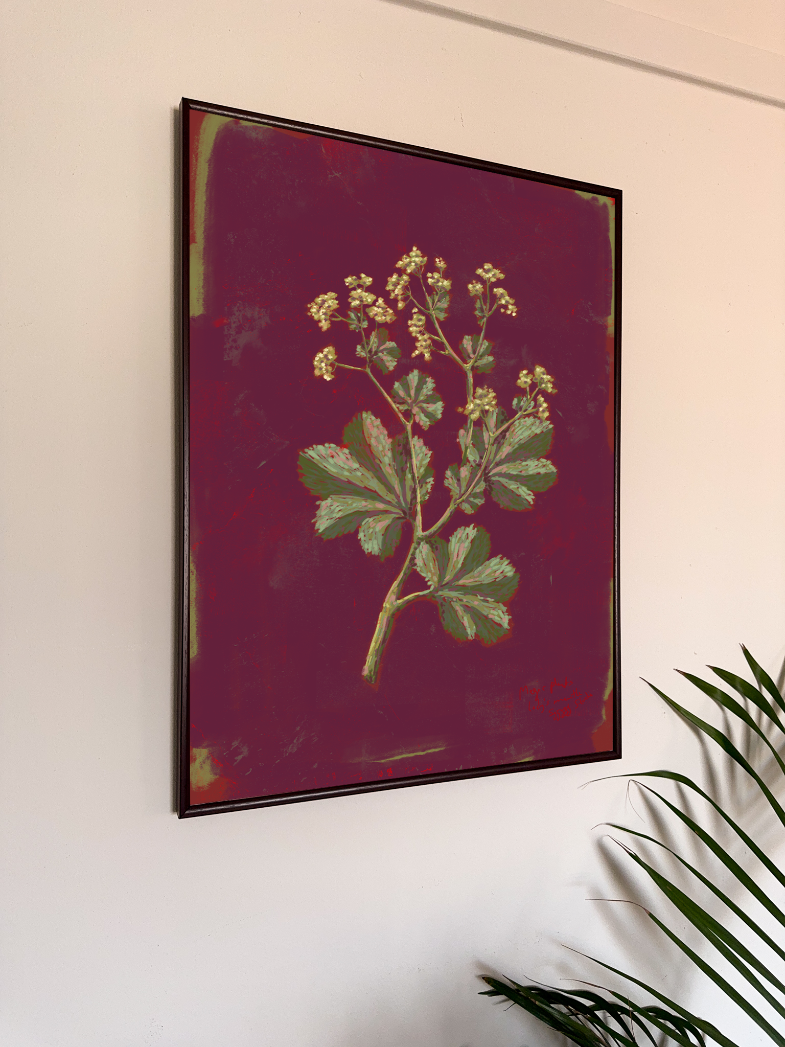 Framed botanical artwork with green leaves and yellow flowers on a dark red background, hanging on a wall.