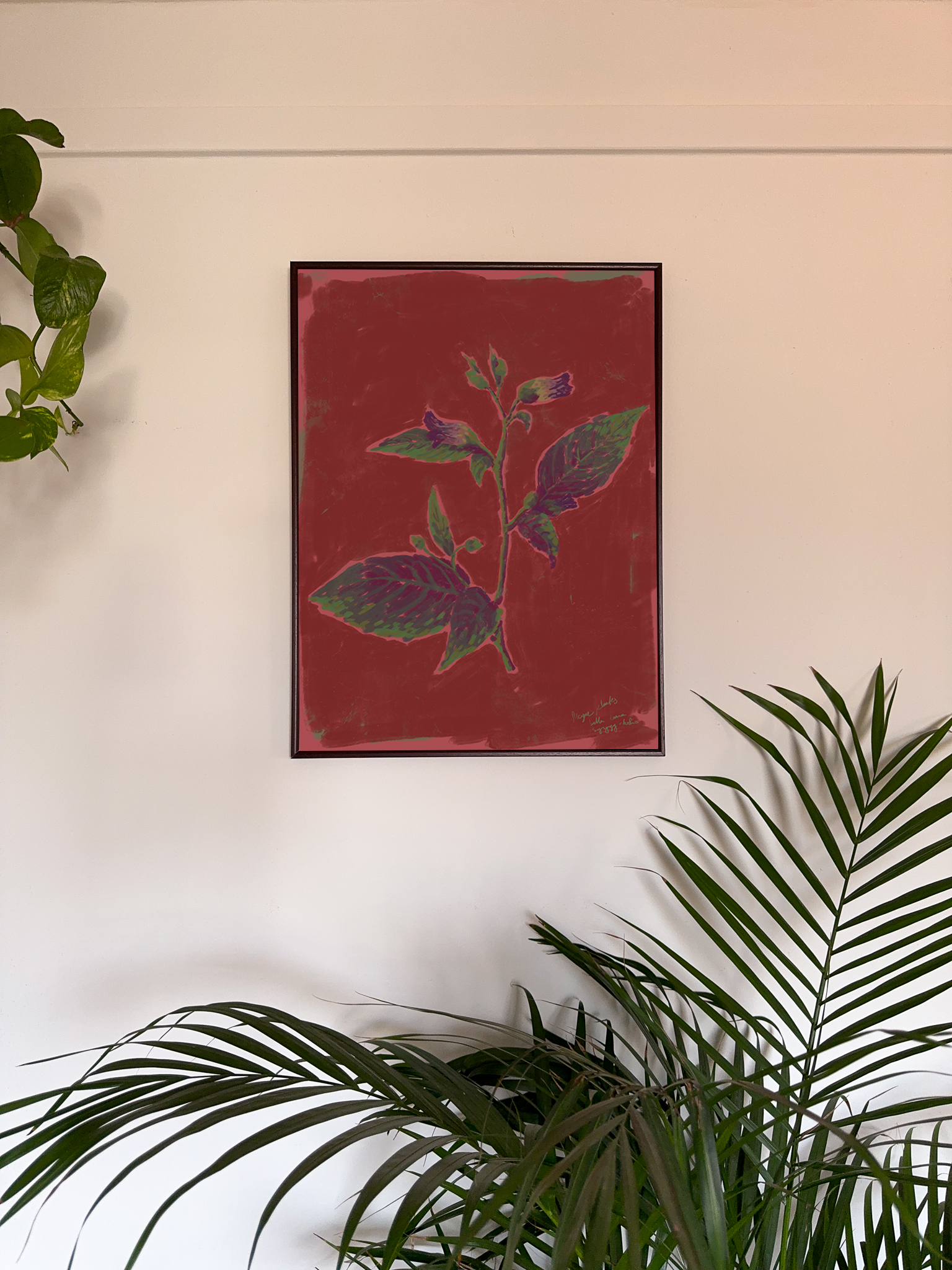 Framed artwork with a flower on a red background and green leaves on a white wall.