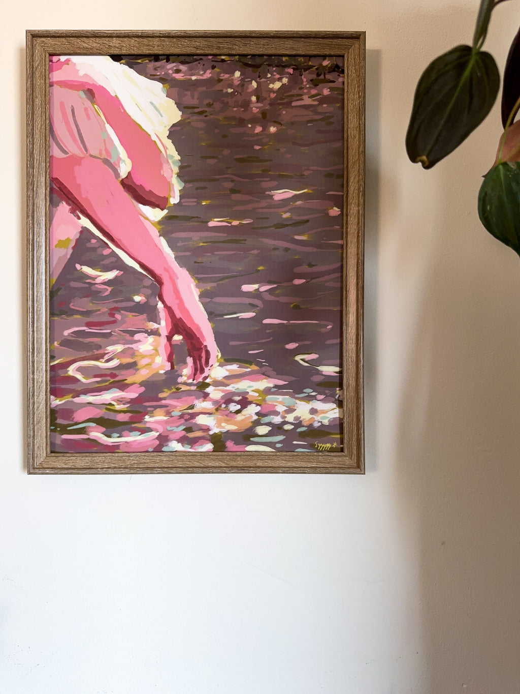 Impressionistic framed art print of a hand touching the water from a boat and sunbeams reflections hanging on a white wall