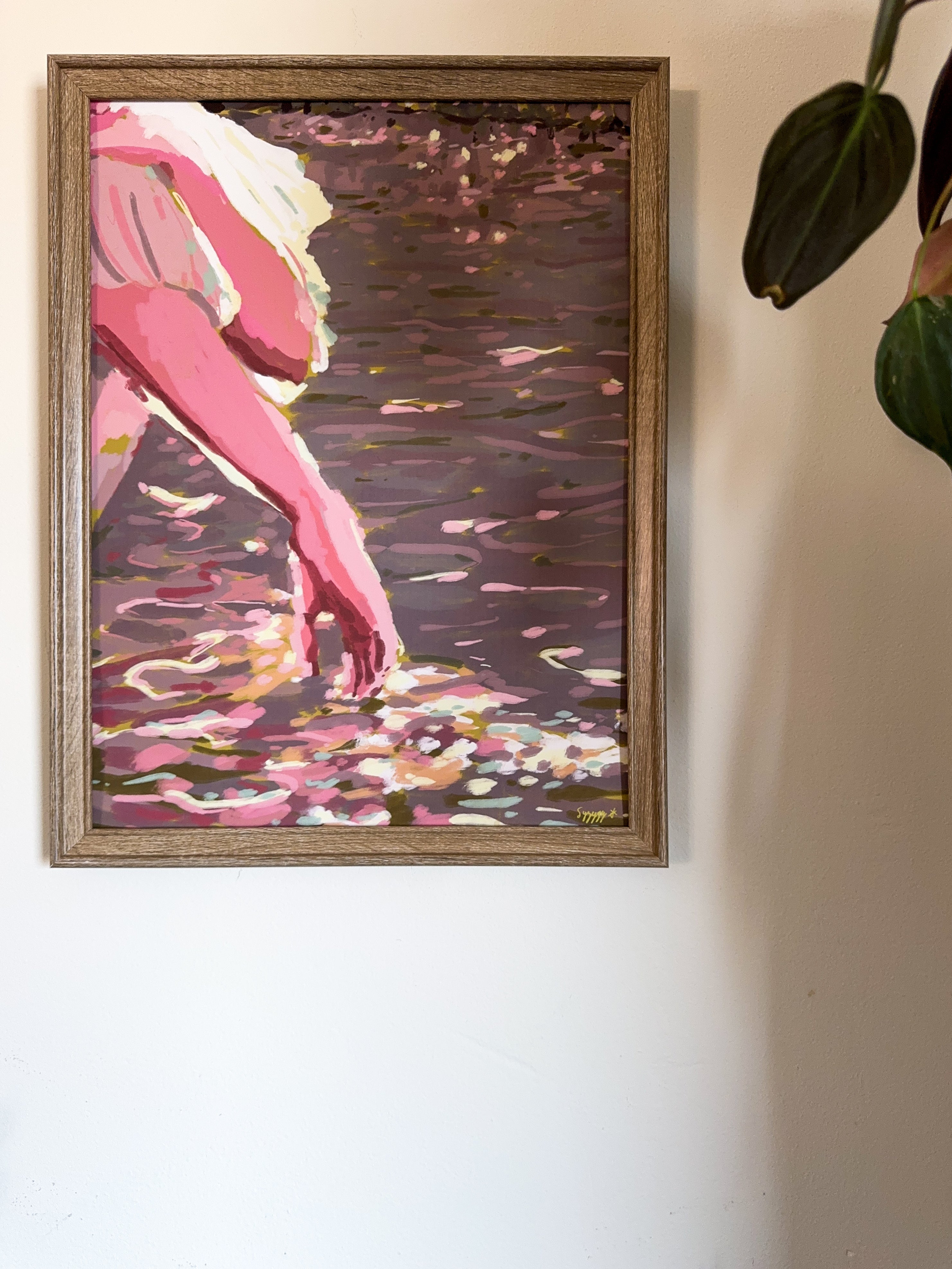 Impressionistic framed art print of a hand touching the water from a boat and sunbeams reflections hanging on a white wall