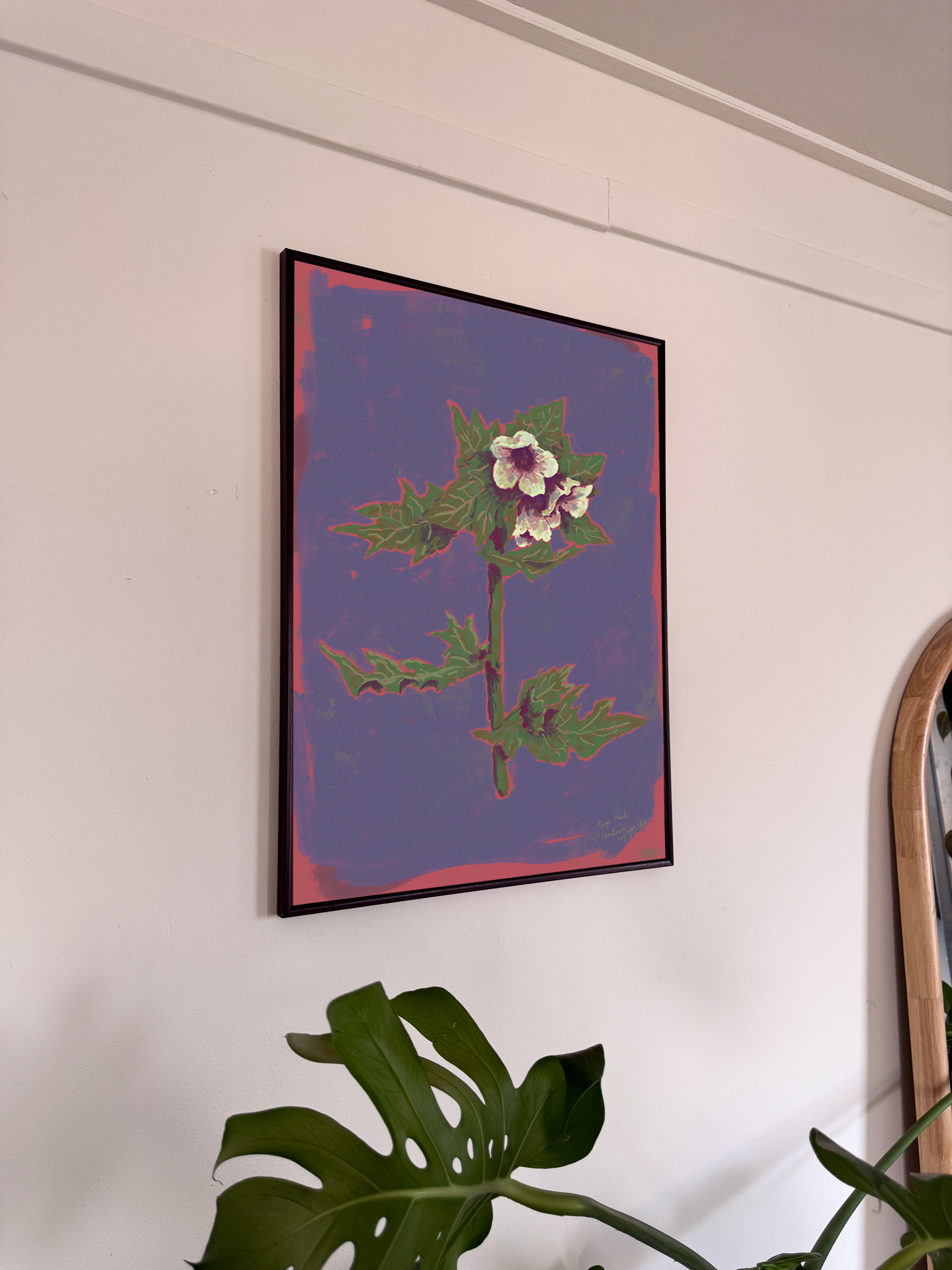 Framed artwork of a purple floral design on a wall with a plant in the foreground.