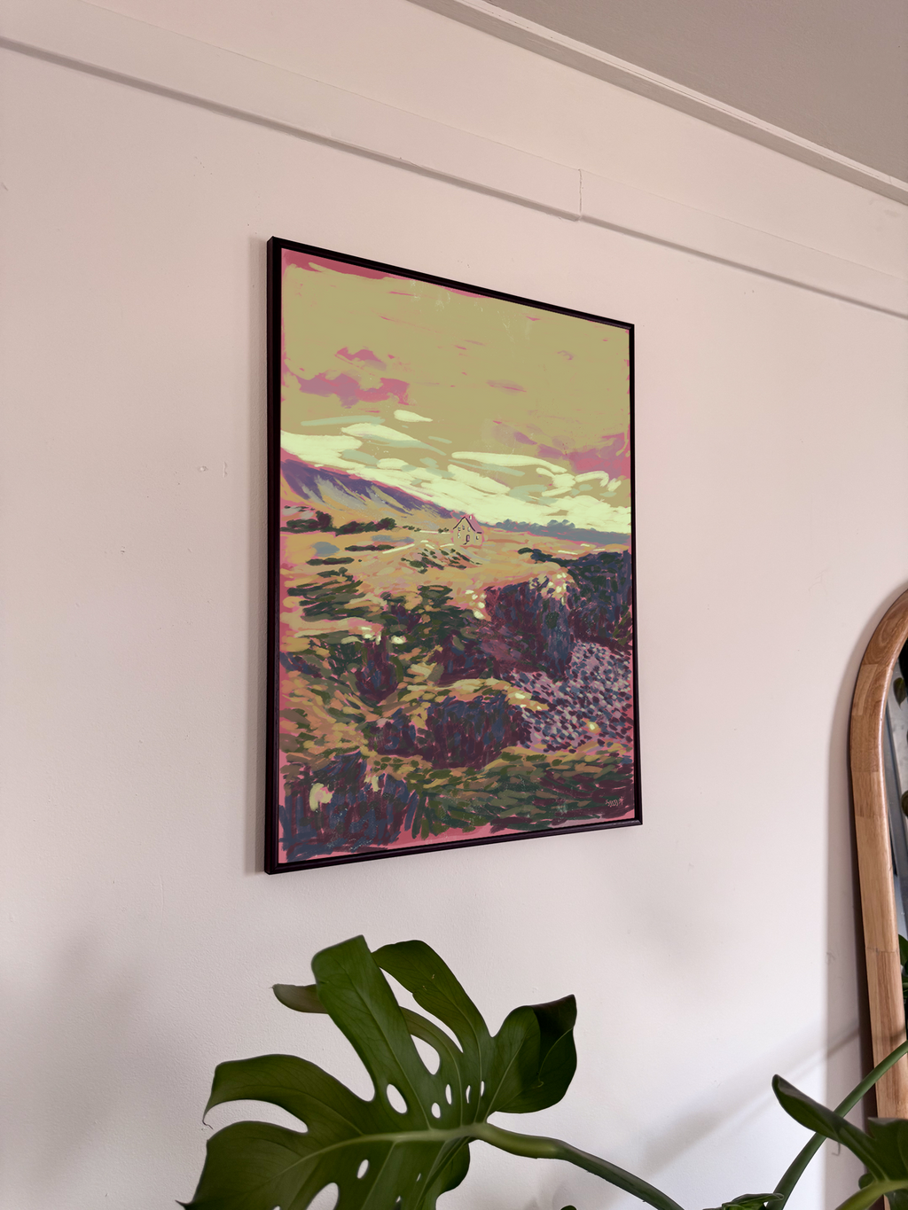 Framed artwork of a landscape with mountains and pink clouds on a white wall.
