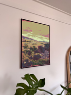Framed artwork of a landscape with mountains and pink clouds on a white wall.