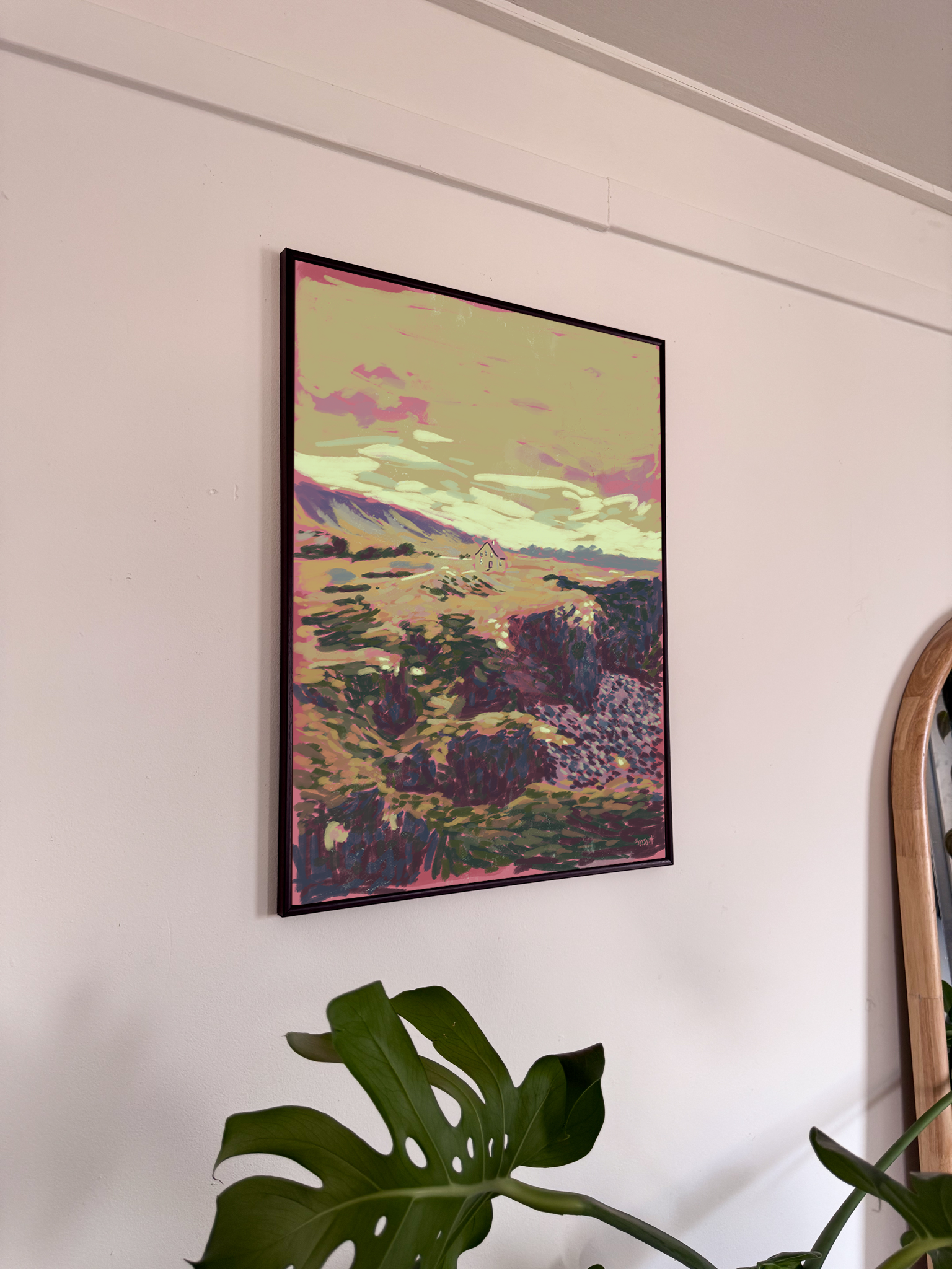 Framed artwork of a landscape with mountains and pink clouds on a white wall.