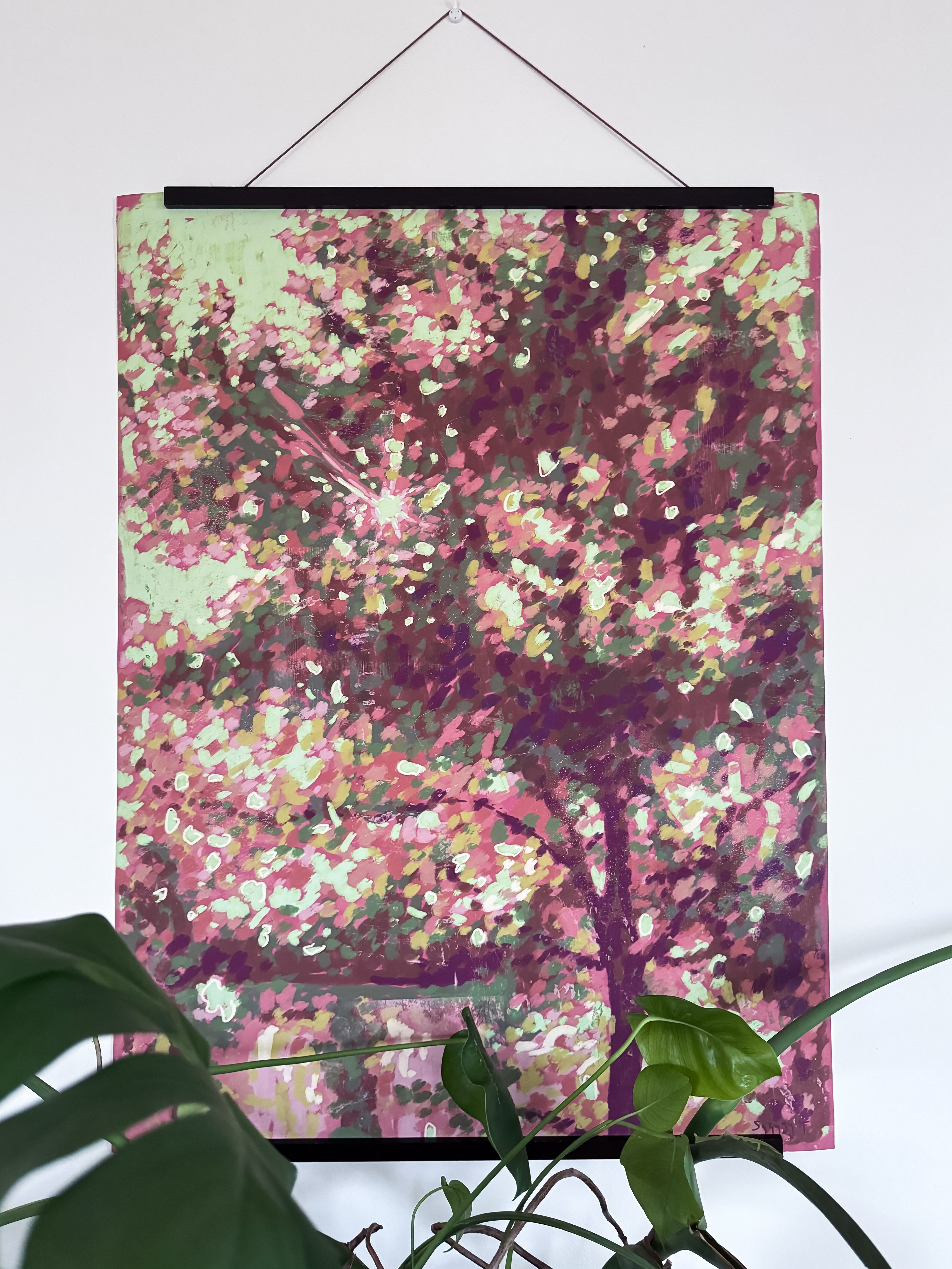 Artwork with hanger of a colorful impressionist tree on a white wall and a plant in the foreground