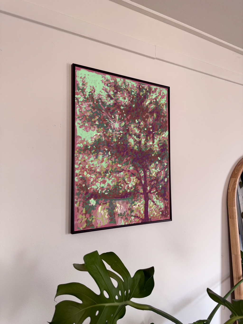 Framed abstract artwork on a wall with a plant in the foreground