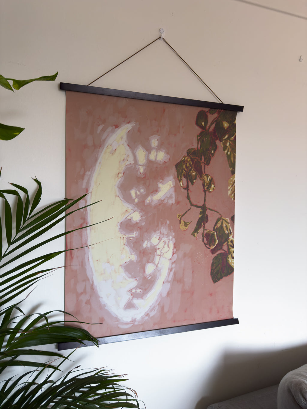 Wall art with a plant and mirror reflection hanging on a white wall.
