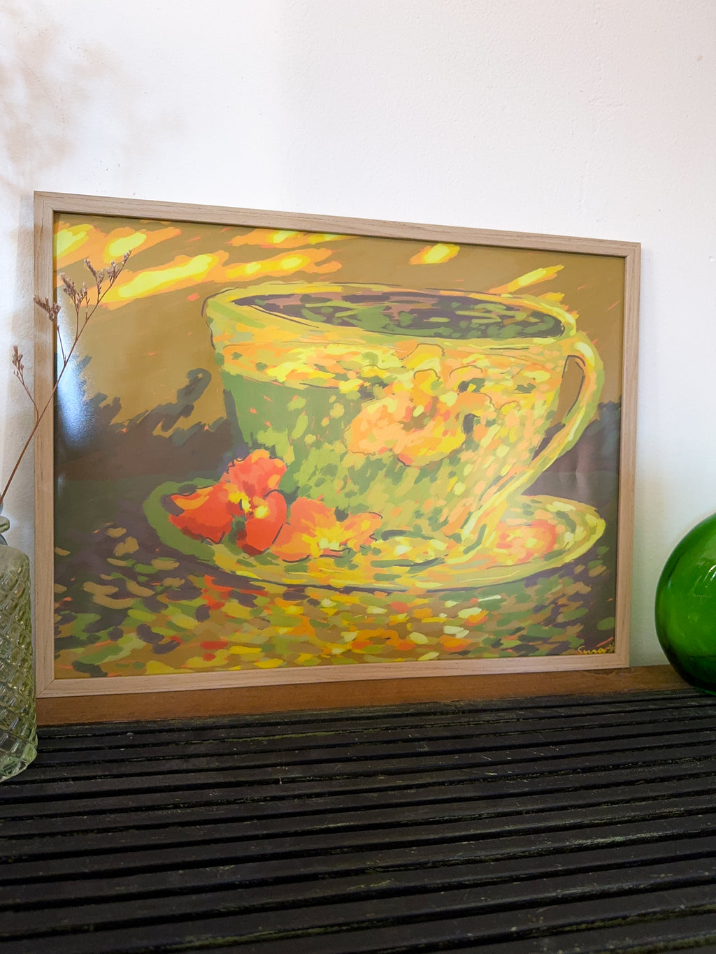 Framed painting of a green teacup with flowers on a wooden surface.