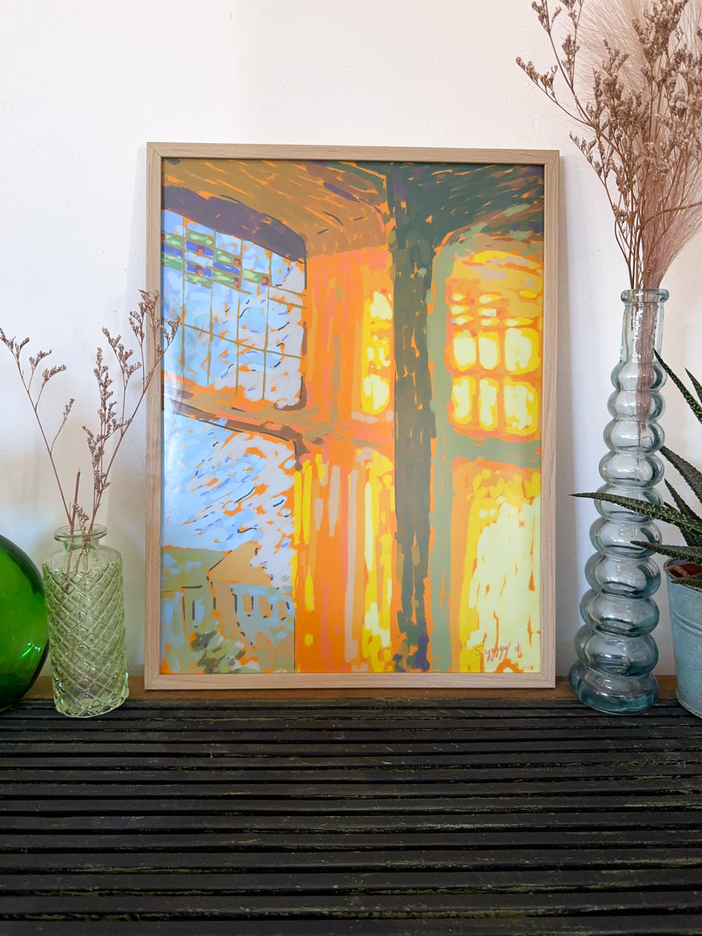 Framed impressionistic art print of sunbeams through a window, on a shelf with decorative vases and plants.