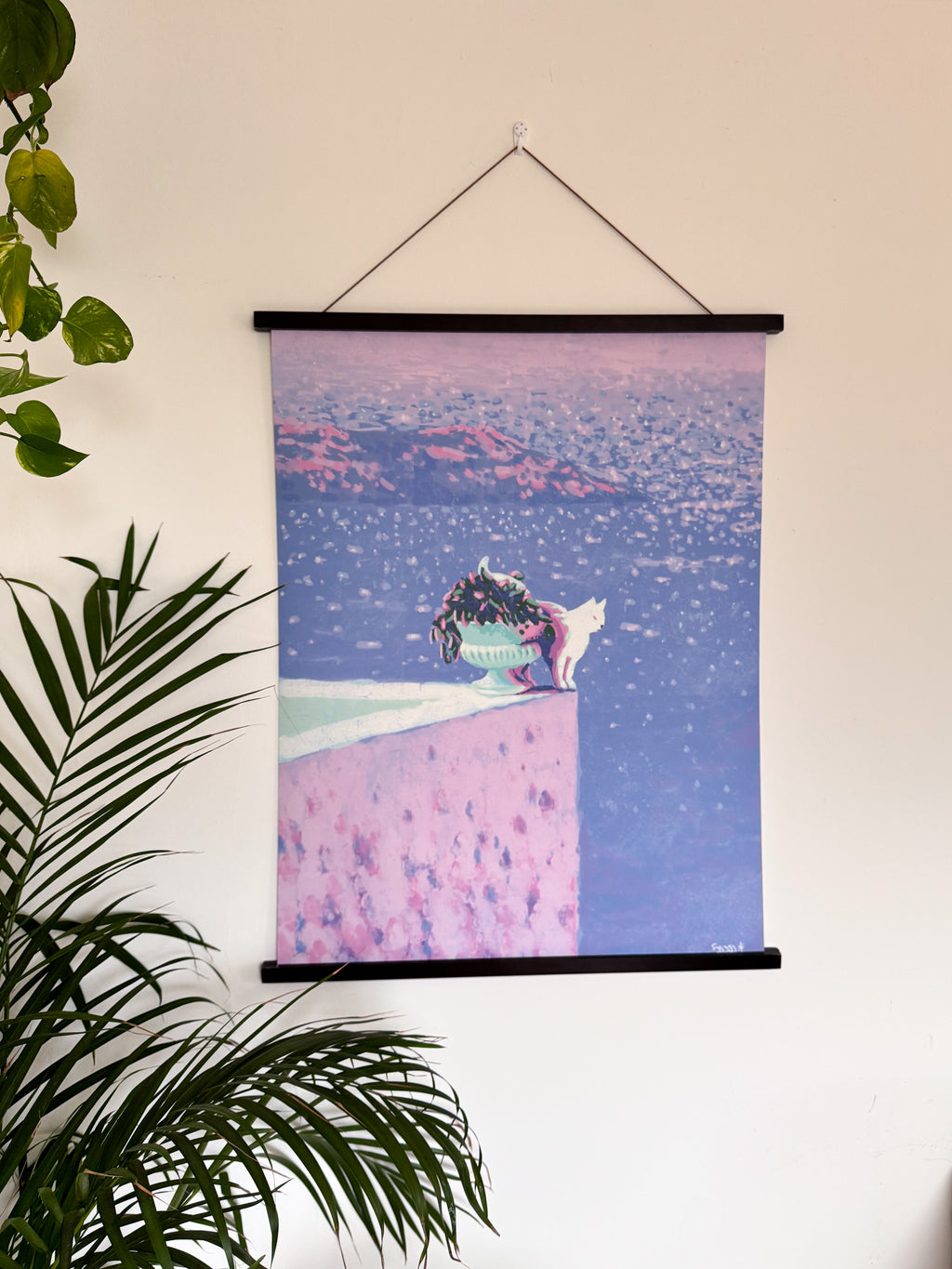 Wall art with a cat on a pink roof terrace and blue sea at the background, hanging on a wall.