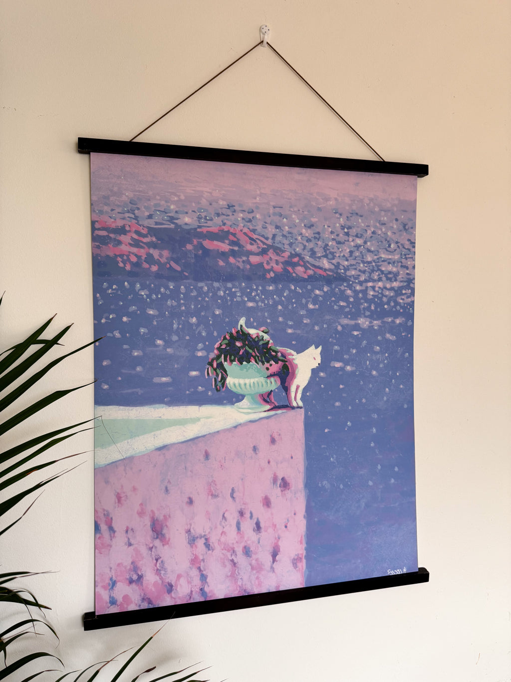 Wall art with a cat on a pink roof terrace and blue sea at the background, hanging on a wall.