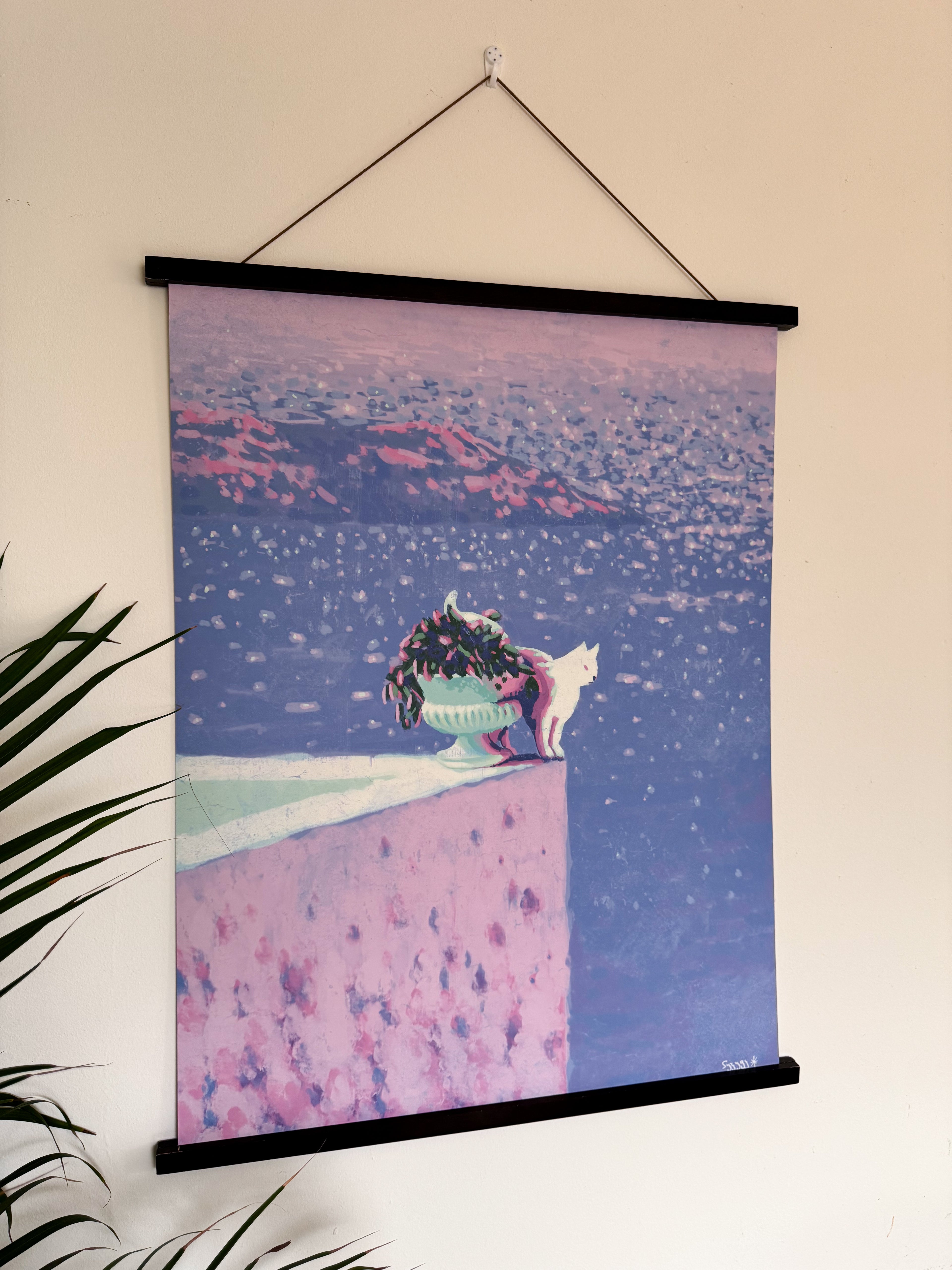 Wall art with a cat on a pink roof terrace and blue sea at the background, hanging on a wall.