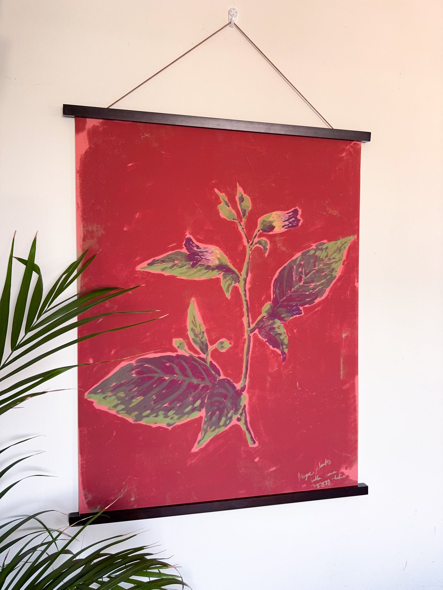 Red wall art print with magnetic hanger, with floral design hanging on a white wall.
