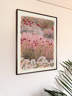 Framed artwork of a floral landscape on a wall with a plant in the foreground.