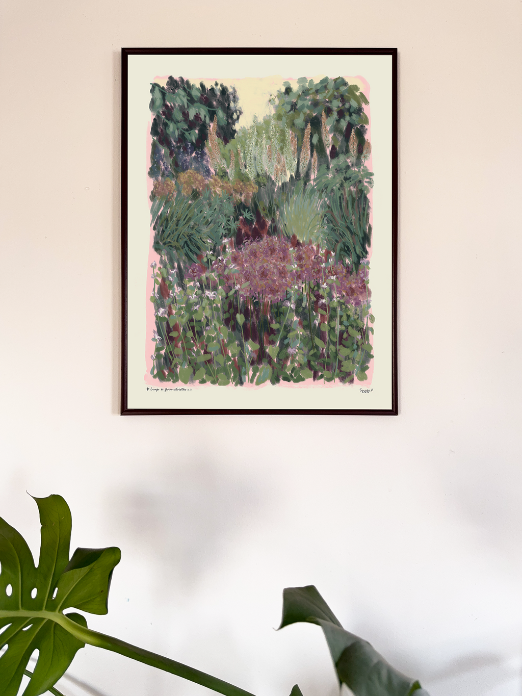 Framed artwork of a garden scene on a wall with a plant in the foreground.
