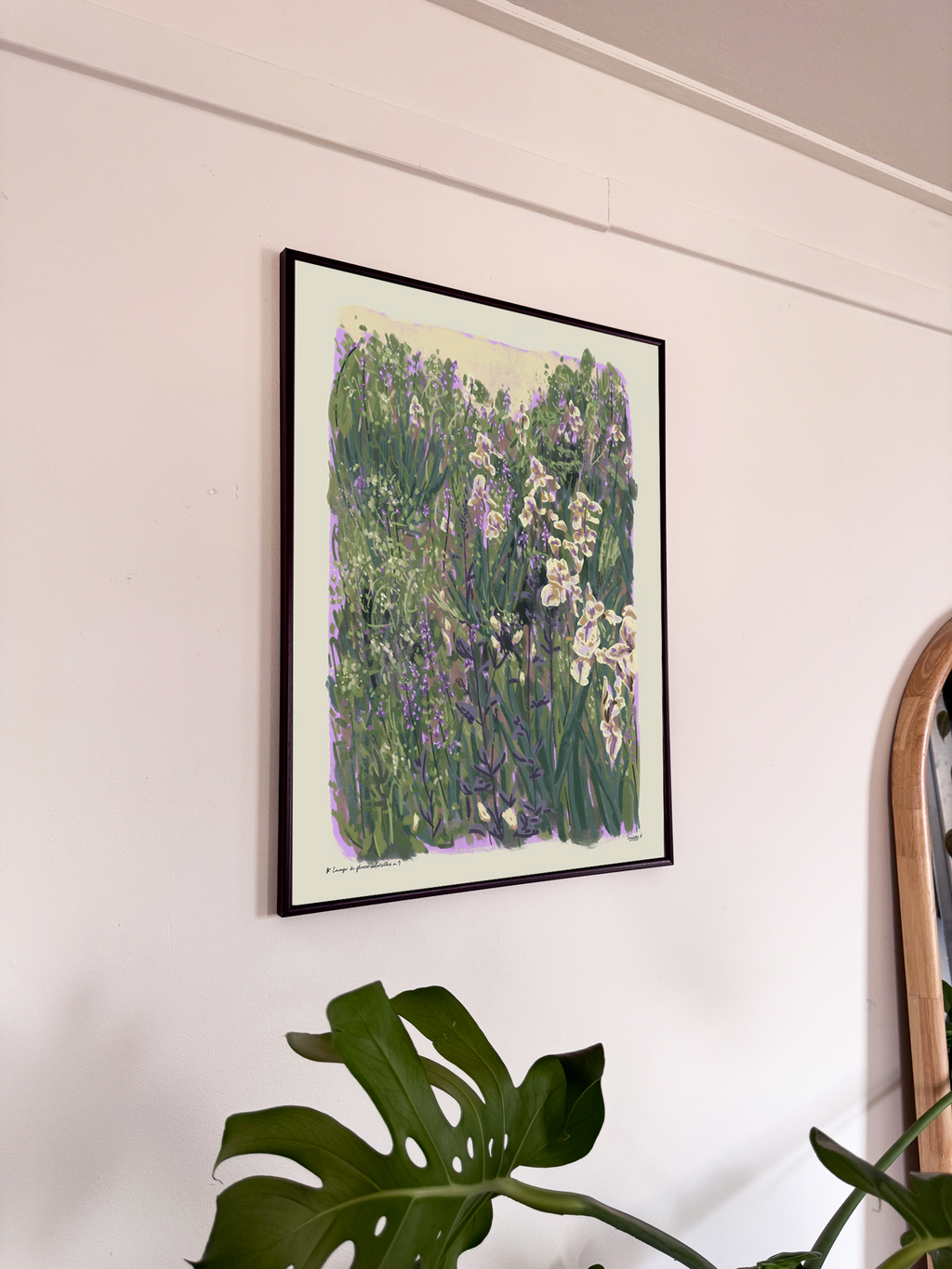 Framed artwork of a garden scene on a wall with a plant in the foreground.