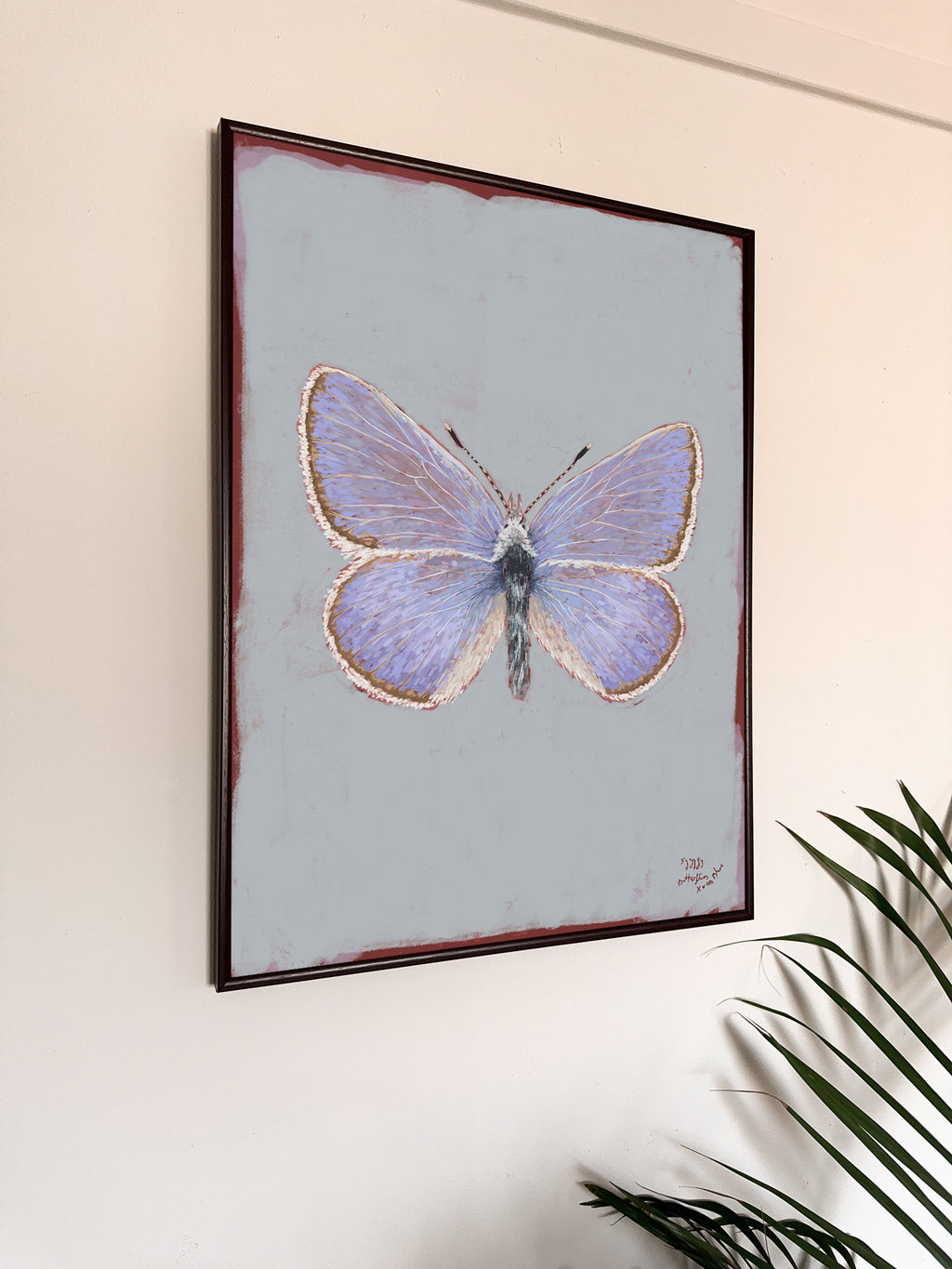 Framed artwork of a butterfly on a light blue background, hanging on a wall.