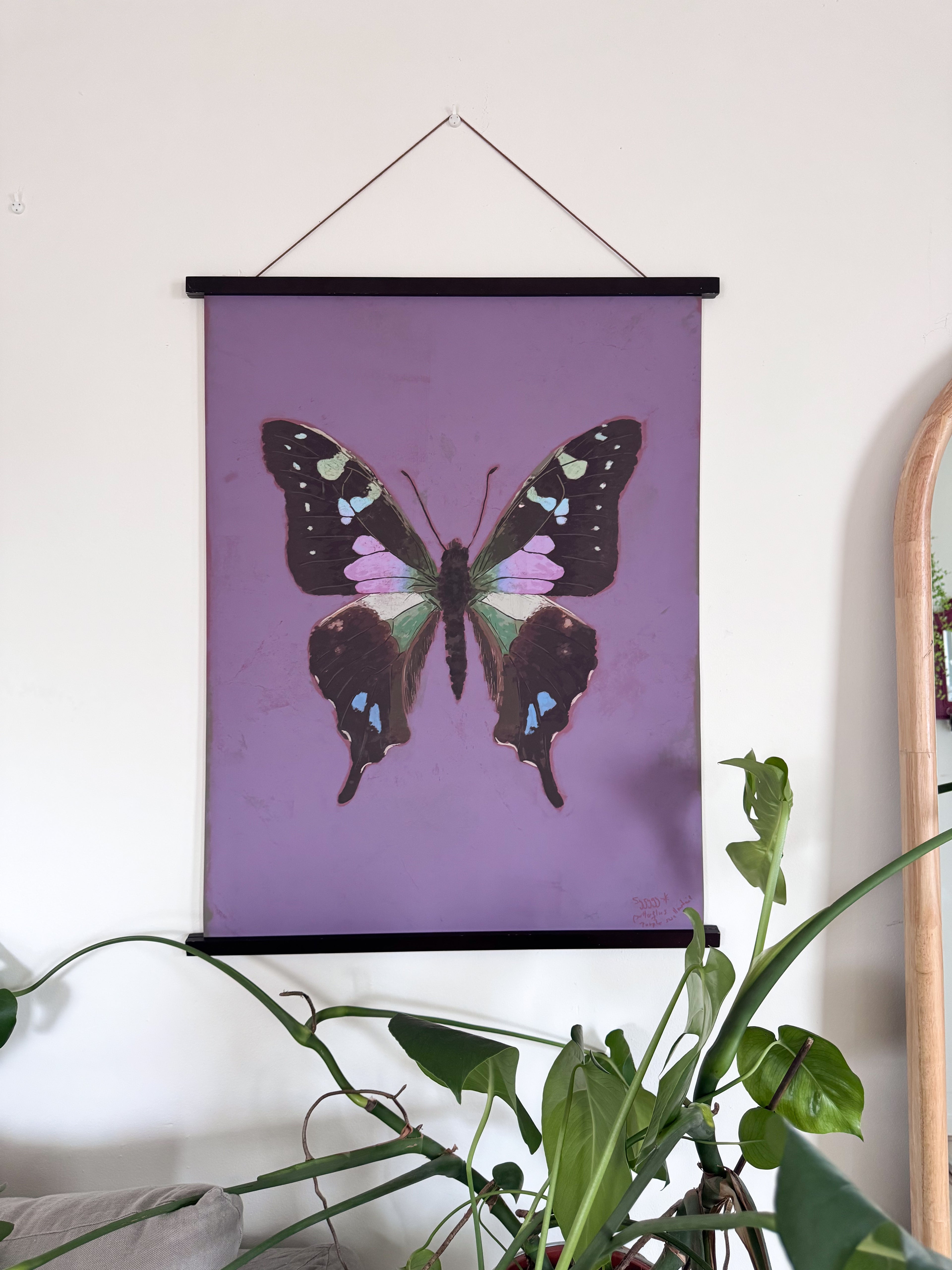 Butterfly poster on a purple background hanging on a wall with plants below.
