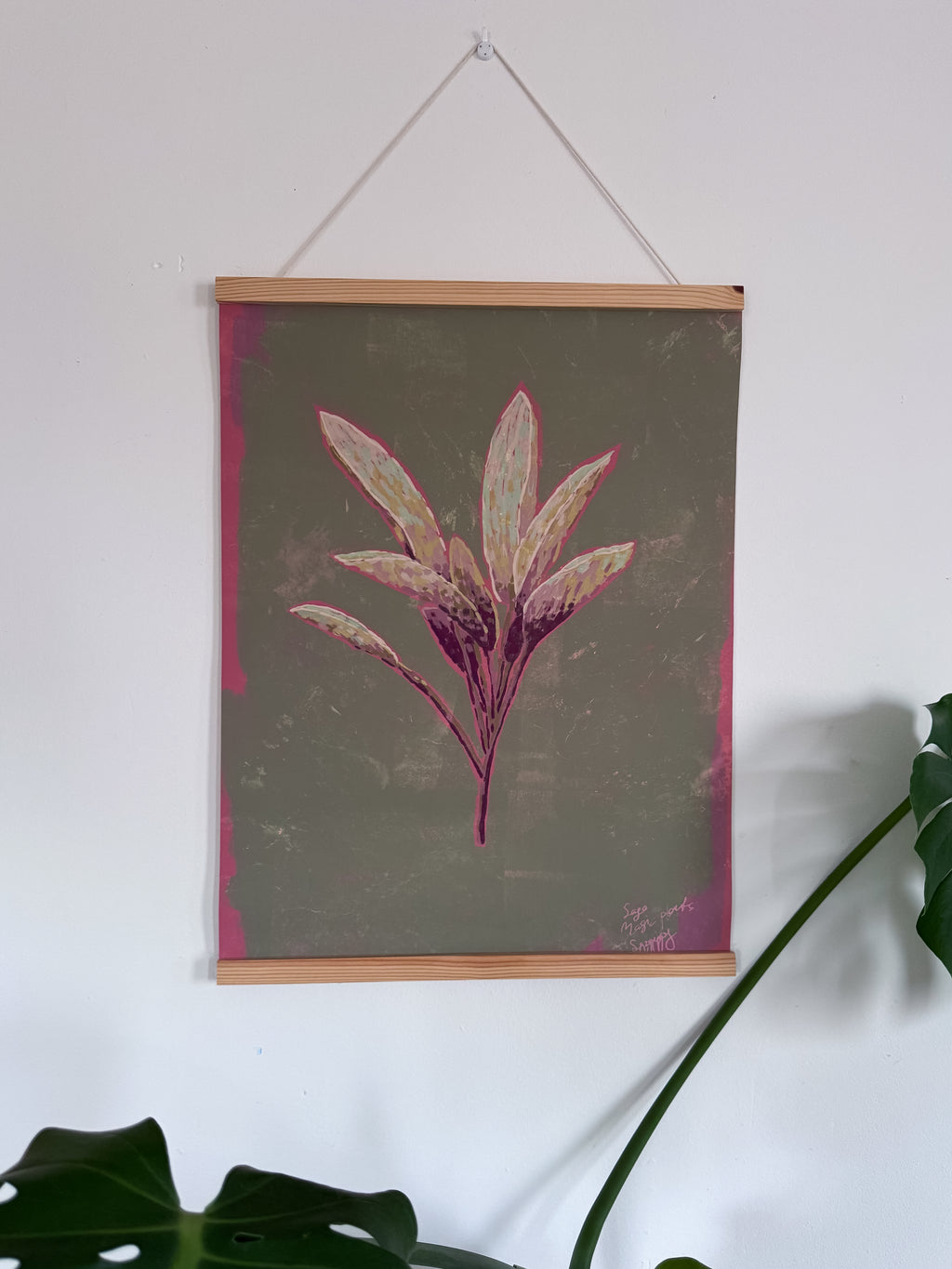 Floral sage artwork with pink leaves in a wooden magnetic frame hanging on a white wall.