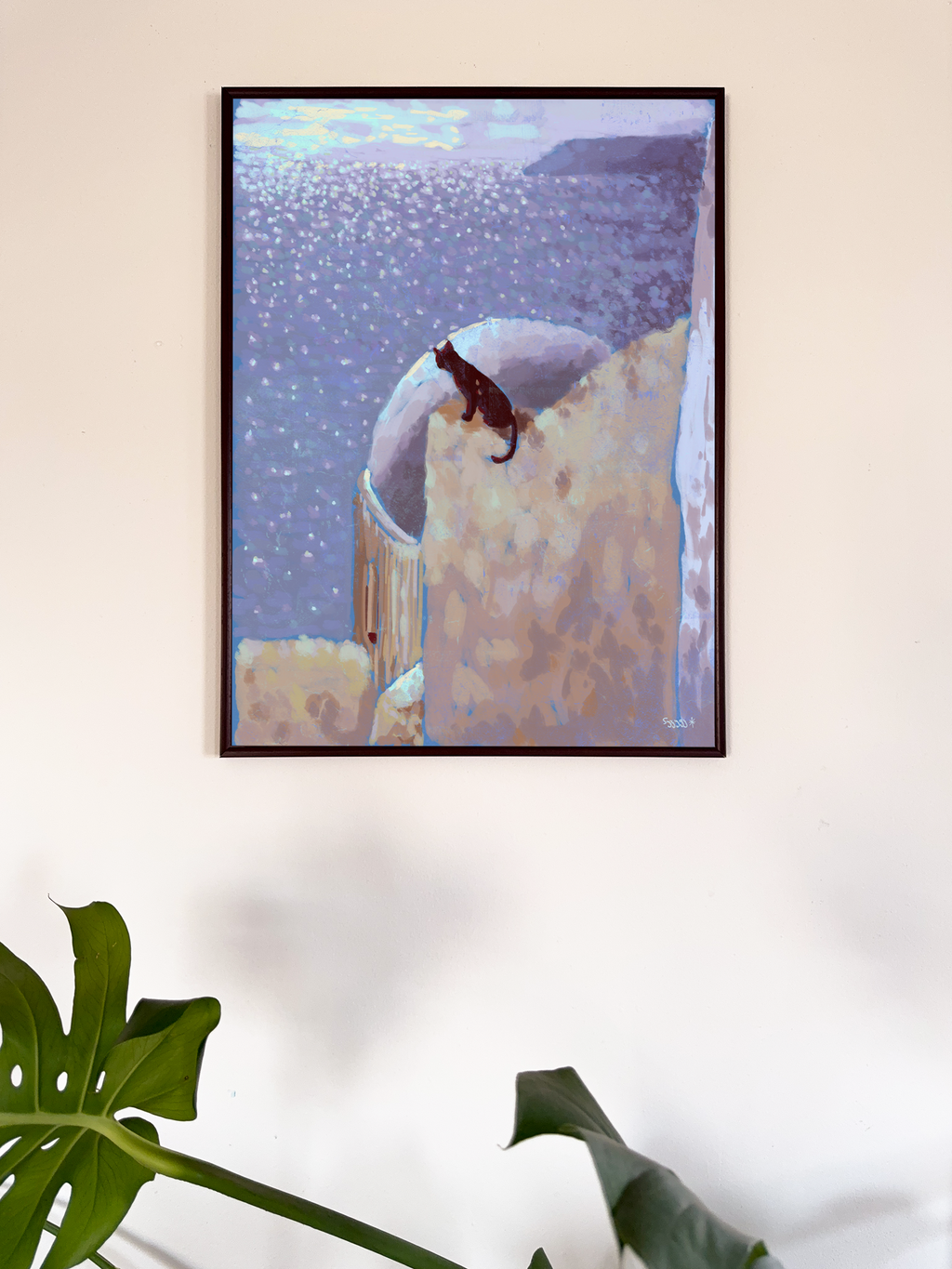 Framed artwork of a cat on a stone wall with the sea at the background, mounted on a wall.